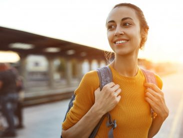 portrait of a young woman traveler with small backpack on the railway stantion. woman waiting for train. Active and travel lifestyle concept